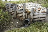Tuyau de régulation du niveau de l'eau dans un marais France ; Le tuyau est stabilisé par des palettes et des gravats.