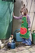 Girl filling his watering can with water from rain France ; Age: 4 years 