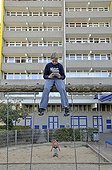 Boy, 9, playing with his Nintendo in front of a high-rise apartment building, satellite town of Chorweiler in Cologne, North Rhine-Westphalia, Germany, Europe