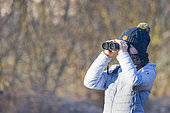 Young girl observing wildlife with binoculars in winter, Côte d'Opale, France