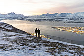 Couple contemplating the fjiord leading to Tromso in the moonlight. View of the city plunged into the polar night from the fjellstua lookout, Tromso, Norway, Arctic