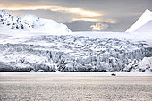 Landscape of Svalbard in Norway, also known as Spitsbergen. This territory stretches from latitude 75 to 80 degrees to the pack ice a few hundred kilometers from the North Pole. Melting ice, early global warming. Front of a glacier fracturing at the edge of a fjord. Explorers' sailboat at the ice edge