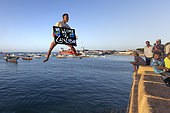 Jeunes plongeurs sautant dans la mer, se faisant filmer tenant des panneaux publicitaires "welcome to Zanzibar" au Sunset Jump Spot, Stone Town, dans la capitale de Zanzibar en Tanzanie