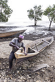 Fisherman repairing his pirogue on a beach at low tide on the east coast of Zanzibar, Tanzania