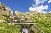 Hiker on a footbridge over a torrent to the Vens lakes, the large upper lake (2325 m), Mercantour National Park, Alpes-Maritimes, France