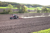 Tractor passing a heavy harrow to refine the soil before sowing, landscape of fields and forest, Lorraine, France