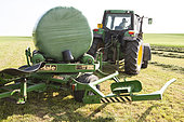 Farmer wrapping round bales of hay in plastic film, France