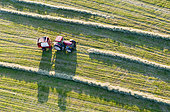 Aerial view of a natural meadow, a farmer baling round bales of hay in the setting sun, haymaking, France