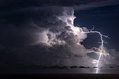 Mediterranean storm, opposite San Remo, Liguria, Italy. An extra-cloudy lightning bolt emerges from a cumulonimbus.