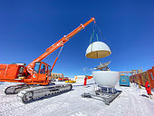 Three technicians assemble the final part of a mobile satellite antenna using a crane. This antenna is used to connect to the Internet at the Beyond Epica drilling camp, located at Little Dome C (about 30 km from the Concordia station). Concordia Antarctic Research Station, Dome C plateau, East Antarctica.