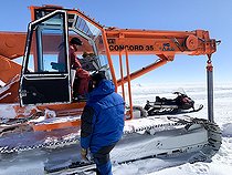 Deux techniciens mécaniciens démarrent la grue après 9 mois d'hiver. L'espace de stockage abrité étant limité, ecrtains véhicules passent l'hiver dehors sous une bâche épaisse. Les fluides qui gèlent, les batteries et autres élements électriques sensibles en sont retirés. A l'été suivant, le compartiment moteur est réchauffé pendant une journée par des chauffages soufflants. Une fois à température, le moteur est démarré puis l'engin est déplacé jusqu'au garage afin d'être mis complètement opérationnel pour la saison estivale. Station de recherche scientifique Antarctique Concordia, plateau du Dôme C, Antarctique de l’Est/oriental.