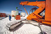 2 technicians assist the transport of an element of the technical tunnel by crane. The metal technical tunnel is designed to carry electrical cables supplying the station's main scientific areas. Concordia Antarctic Research Station, Dome C plateau, East Antarctica.