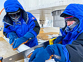 Two scientists perform a series of measurements on a piece of snow to determine its structure, hardness, etc. near the feet of the Concordia station. Concordia Antarctic Research Station, Dome C plateau, East Antarctica.