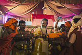 Kumbh Mela 2025: The Sacred Goes Viral. Pilgrims Taking Photos During the Rudrabhishek Ritual. Swamy Gnana Prasanna Giri and Pilgrims Capturing Moments During the Rudrabhishek Ritual. During the sacred Rudrabhishek ritual, which involves the worship of Lord Shiva through chanting and offerings, pilgrims participate not only in the spiritual experience but also in documenting it. The image captures pilgrims holding their smartphones to take selfies and photos, blending the ancient tradition with modern technology. Swamy Gnana Prasanna Giri, affectionately known as 'Guruvu garu' by his followers, is also present, leading the ceremony. The colorful lighting and the energy of the devotees contrast with the deep reverence of the ritual, highlighting how technology has become an integral part of documenting spiritual experiences.