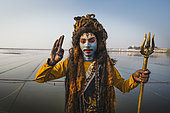 Kumbh Mela 2025: The Sacred Goes Viral. Sadhu Posing as Lord Shiva by the River at the Kumbh Mela. A sadhu, dressed as Lord Shiva, stands by the river during the Kumbh Mela, striking a pose with a trident in hand. His face painted with the iconic blue and white markings of Shiva, he embodies the divine presence of the Hindu god of destruction and transformation. The sacred river flows peacefully behind him, symbolizing the purity and spiritual power that attracts millions of devotees to the Kumbh Mela. The sadhu’s pose, with his hand raised in blessing, exemplifies the devotion and connection that many pilgrims feel as they engage in rituals and worship during this sacred event. The image captures the intersection of faith, tradition, and the rich cultural diversity that defines the Kumbh Mela.