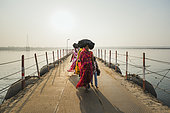 Kumbh Mela 2025: The Sacred Goes Viral. Women Crossing the Bridge with Their Bags on Their Heads at Suns. At sunset, a group of women walks across the bridge, balancing their bags gracefully on their heads. The warm glow of the setting sun casts a beautiful light over the scene, creating a serene and peaceful atmosphere. The women, dressed in traditional attire, are part of the vast movement of pilgrims at the Kumbh Mela, each carrying their belongings and personal stories. Balancing heavy bags on their heads is a common practice in many parts of India, symbolizing strength, grace, and resilience. The image captures the quiet beauty of everyday life at the Kumbh Mela, where even the simplest actions take on profound meaning in the context of faith, tradition, and community.