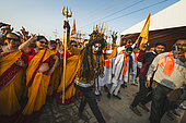 Kumbh Mela 2025: The Sacred Goes Viral. Celebrating at the Kumbh Mela with Devotees Dancing and a Sadhu. Devotees and a Sadhu Dancing and Celebrating at the Kumbh Mela. A joyful scene at the Kumbh Mela where devotees, dressed in white and adorned with orange scarves, celebrate in unison, dancing to the rhythm of spiritual music and chanting. In the center of the crowd, a sadhu dressed as a divine figure, with painted face and long hair, becomes part of the celebration, embodying the spiritual energy that the festival exudes. The lively expressions and movements of the devotees contrast with the more serene aspects of the Kumbh, showing how spirituality and celebration blend at this unique gathering. The image captures a moment of unity, devotion, and joy, as people from all walks of life come together, celebrating their faith and the shared experience of the Kumbh Mela.