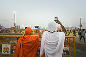Kumbh Mela 2025: The Sacred Goes Viral. Sadhu Taking Photos at the Kumbh Mela. Sadhu Capturing the Moment on Their Phones at the Kumbh Mela. At the Kumbh Mela, two sadhu, dressed in traditional attire, capture the vibrant scene unfolding before them, holding smartphones to take photos. The contrast between the ancient spiritual practices of the sadhus and the modern technology of smartphones highlights the evolving nature of faith in the digital age. While the sacred ritual continues, the sadhu’s use of technology symbolizes how spirituality and modern life coexist at this grand gathering. The photo perfectly captures the merging of traditional devotion with the use of social media to document the extraordinary scale and energy of the festival.