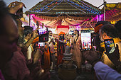 Kumbh Mela 2025: The Sacred Goes Viral. Pilgrims Taking Photos During the Rudrabhishek Ritual. Swamy Gnana Prasanna Giri and Pilgrims Capturing Moments During the Rudrabhishek Ritual. During the sacred Rudrabhishek ritual, which involves the worship of Lord Shiva through chanting and offerings, pilgrims participate not only in the spiritual experience but also in documenting it. The image captures pilgrims holding their smartphones to take selfies and photos, blending the ancient tradition with modern technology. Swamy Gnana Prasanna Giri, affectionately known as 'Guruvu garu' by his followers, is also present, leading the ceremony. The colorful lighting and the energy of the devotees contrast with the deep reverence of the ritual, highlighting how technology has become an integral part of documenting spiritual experiences.