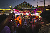 Kumbh Mela 2025: The Sacred Goes Viral. Pilgrims Taking Photos During the Rudrabhishek Ritual. During the sacred Rudrabhishek ritual, which involves the worship of Lord Shiva through chanting and offerings, pilgrims participate not only in the spiritual experience but also in documenting it. The image captures pilgrims holding their smartphones to take selfies and photos, blending the ancient tradition with modern technology. Swamy Gnana Prasanna Giri, affectionately known as 'Guruvu garu' by his followers, is also present, leading the ceremony. The colorful lighting and the energy of the devotees contrast with the deep reverence of the ritual, highlighting how technology has become an integral part of documenting spiritual experiences.