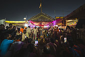 Kumbh Mela 2025: The Sacred Goes Viral. Pilgrims Taking Photos During the Rudrabhishek Ritual. Swamy Gnana Prasanna Giri and Pilgrims Capturing Moments During the Rudrabhishek Ritual. During the sacred Rudrabhishek ritual, which involves the worship of Lord Shiva through chanting and offerings, pilgrims participate not only in the spiritual experience but also in documenting it. The image captures pilgrims holding their smartphones to take selfies and photos, blending the ancient tradition with modern technology. Swamy Gnana Prasanna Giri, affectionately known as 'Guruvu garu' by his followers, is also present, leading the ceremony. The colorful lighting and the energy of the devotees contrast with the deep reverence of the ritual, highlighting how technology has become an integral part of documenting spiritual experiences.