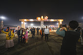 Kumbh Mela 2025: The Sacred Goes Viral. The Gateway of Kumbh Mela: A Gathering of Pilgrims and Devotees. Pilgrims and Devotees Preparing to Enter the Kumbh Mela Grounds, Captured Under the Night Lights. A vibrant scene at the Kumbh Mela where pilgrims and devotees walk through a brightly lit gateway. People are seen taking selfies and photos while others join the crowd heading towards the sacred site. The iconic entrance illuminated at night welcomes thousands to the largest spiritual gathering in the world. This image captures the fusion of tradition and modernity, as people from all walks of life engage with the festival, blending devotion and contemporary social media culture.