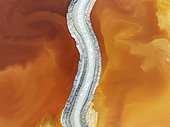 Track crossing a waste pond in the mineral-rich area of the Rio Tinto mines. The colour is caused by oxidised iron minerals. Aerial view. Drone shot. Huelva province, Andalusia, Spain.