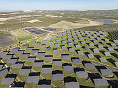 Rows of solar panels at a photovoltaic plant and the town of Espejo in the distance. Aerial view. Drone shot. Córdoba province, Andalucía, Spain.