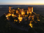 The impressive eighth-century Moorish castle of Almodóvar del Río perches high above the Guadalquivir river valley. Floodlit at dusk. Aerial view. Drone shot. Córdoba province, Andalusia, Spain.