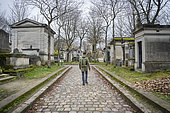 A man seen from behind walking alone in an alley of the Pere Lachaise cemetery in the 20th arrondissement of Paris, France