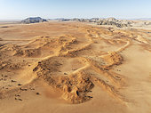 Sand dunes grown with camelthorn trees (Vachellia erioloba) and isolated mountain ridges in the Tsondab Valley in the Namib Desert. Aerial view. Drone shot. Namibia.