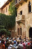 Tourists gather in the courtyard of Juliet's house and a young lady stands on the famous balcony. In fact the building was 'creatively' restored in the 1930s to create its current romantic appearence. Verona, Veneto, Italy