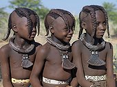 Namibia;Kaokoland - Three young girls, their bodies lightly smeared with a mixture of red ochre, butterfat and herbs, wear round white-beaded necklaces, called ombwari, a tradition of all Himba people. Their other neck ornaments, eha, are made of le [...]