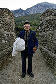 A serene old farmer poses for a portrait just before crossing a bridge made of ropes and wood over the River Vjosa, Valley of Permet, Albania
