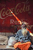 A Sadu (holy man) sits in stark contrast with the ad behind him in the alleys of Varanasi.