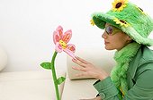 Studio shot of young brunette woman in grass and flower costume and hat looking at artificial flower