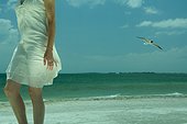 Woman walking on beach, gull flying in background