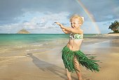 Hawaii, Oahu, Young girl in a hula skirt dancing on the beach, rainbow in background.