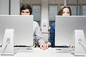 young couple sitting behind computers in office holding hands