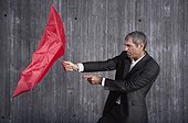 businessman trying to hold red umbrella in stormy weather