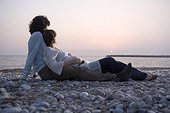 Young couple lying on beach, woman pregnant, sunset