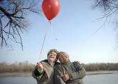 Senior couple by river holding red balloon, smiling