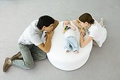Young parents leaning against ottoman, looking at baby lying between them