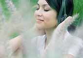 Woman listening to headphones, vegetation in foreground