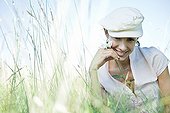 Woman sitting in tall grass, holding flower, smiling at camera
