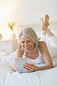 Senior woman lying on bed and using digital tablet